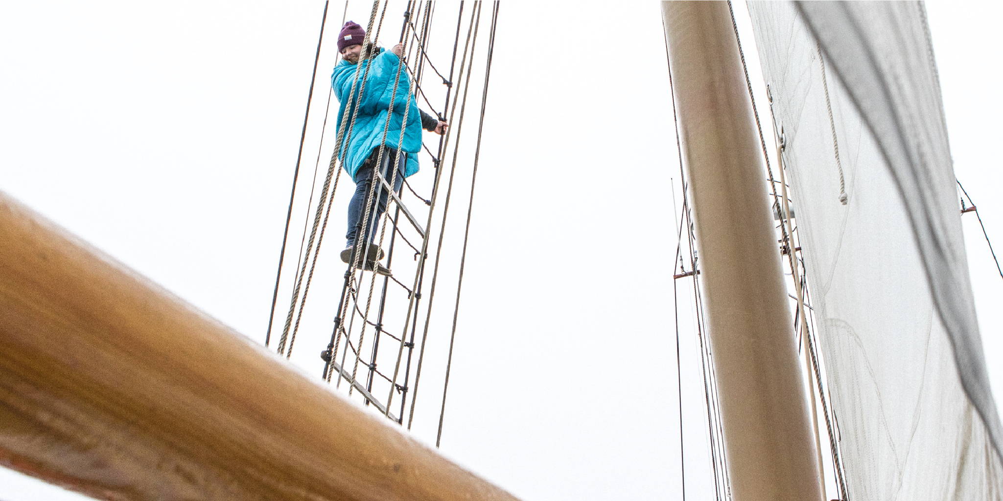 Man climbing up the rope ladder on a sail boat wrapped in a blue rumpl blanket