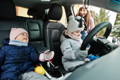 Children sitting in an electric car wearing winter clothes.