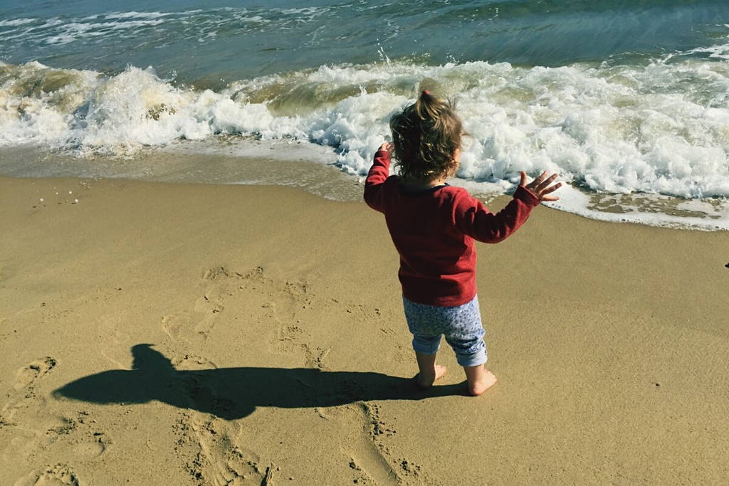 Little girl waiting for waves with open hands close to water.