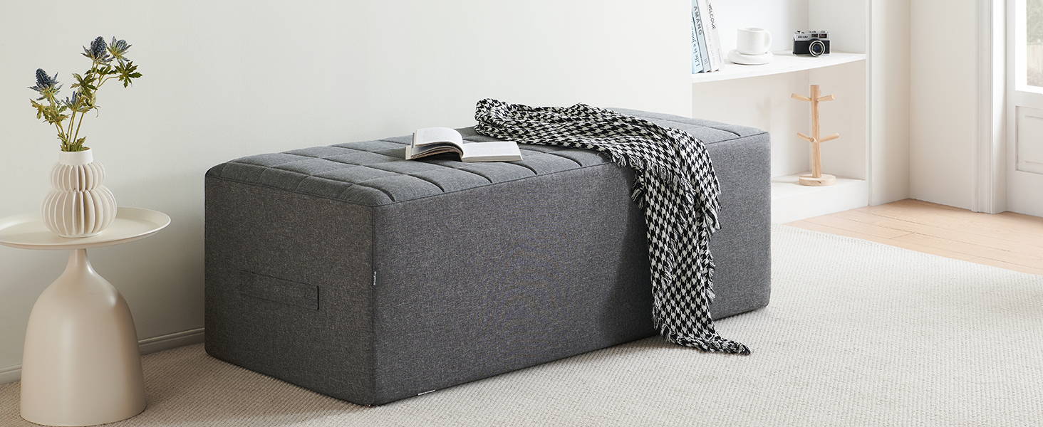 A piece of black-and-white fabric and a book lie on the grey Inofia three-fold mattress, which has been neatly folded away and placed in the living room