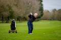 Senior golfer taking a full swing with a golf bag cart nearby.
