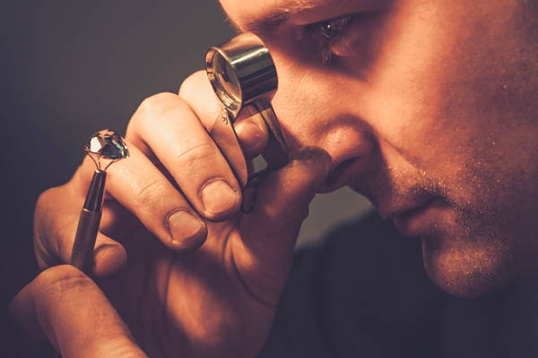 Un joaillier regarde un bijou funéraire à l'aide d'une loupe de joaillerie.