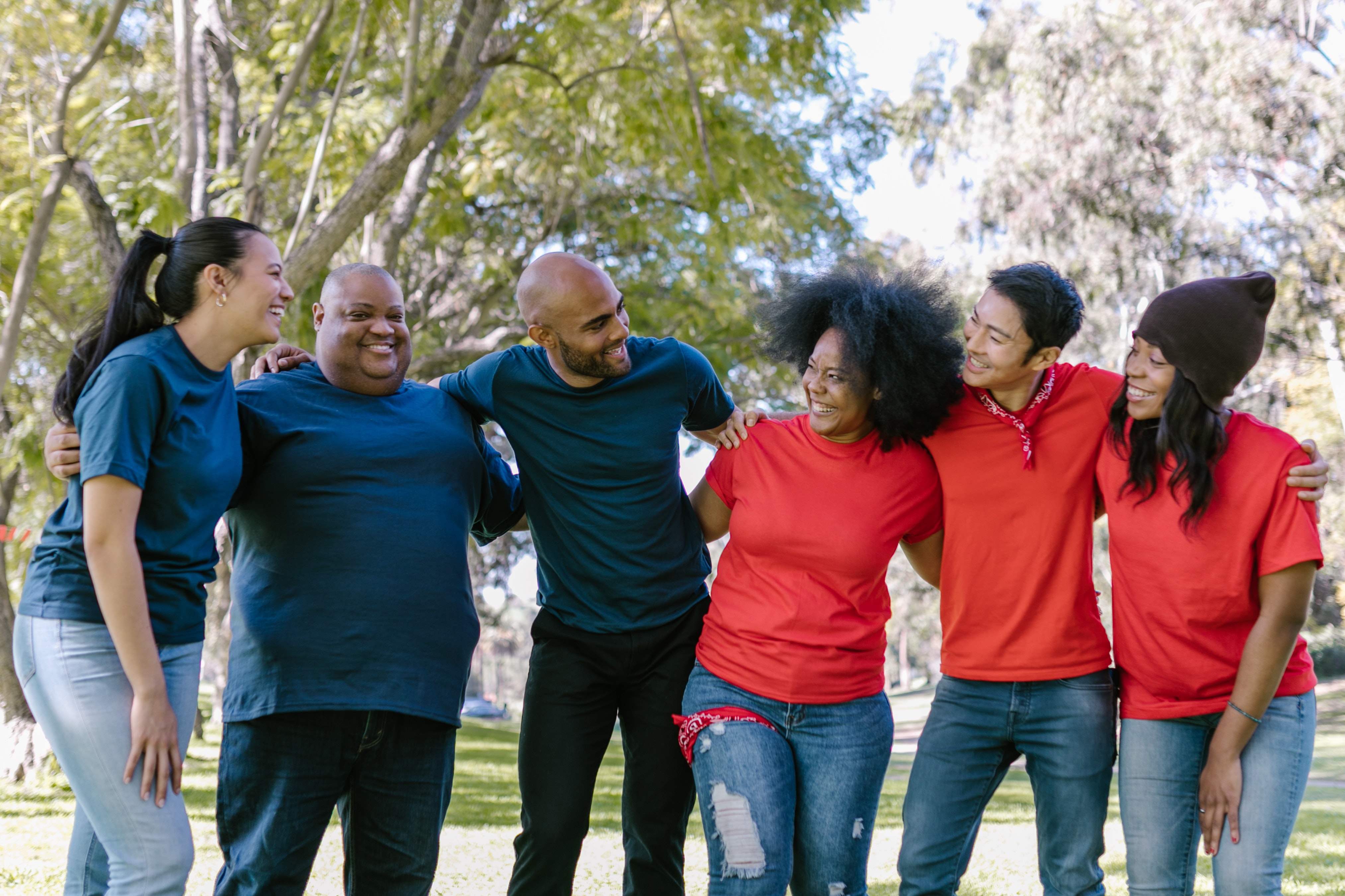 A group of several multi ethnic people all locked arms and wearing blue and red t shirts depending on their team. They are all laughing and smiling.