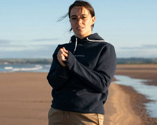 Woman on a scottish beach wearing navy blue organic cotton hoodie from sustainable outdoor brand Meander