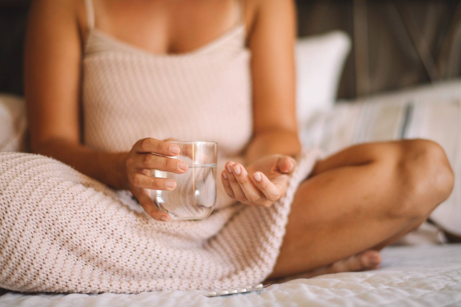 Frau im Bett mit Wasserglas und Kapseln in der Hand