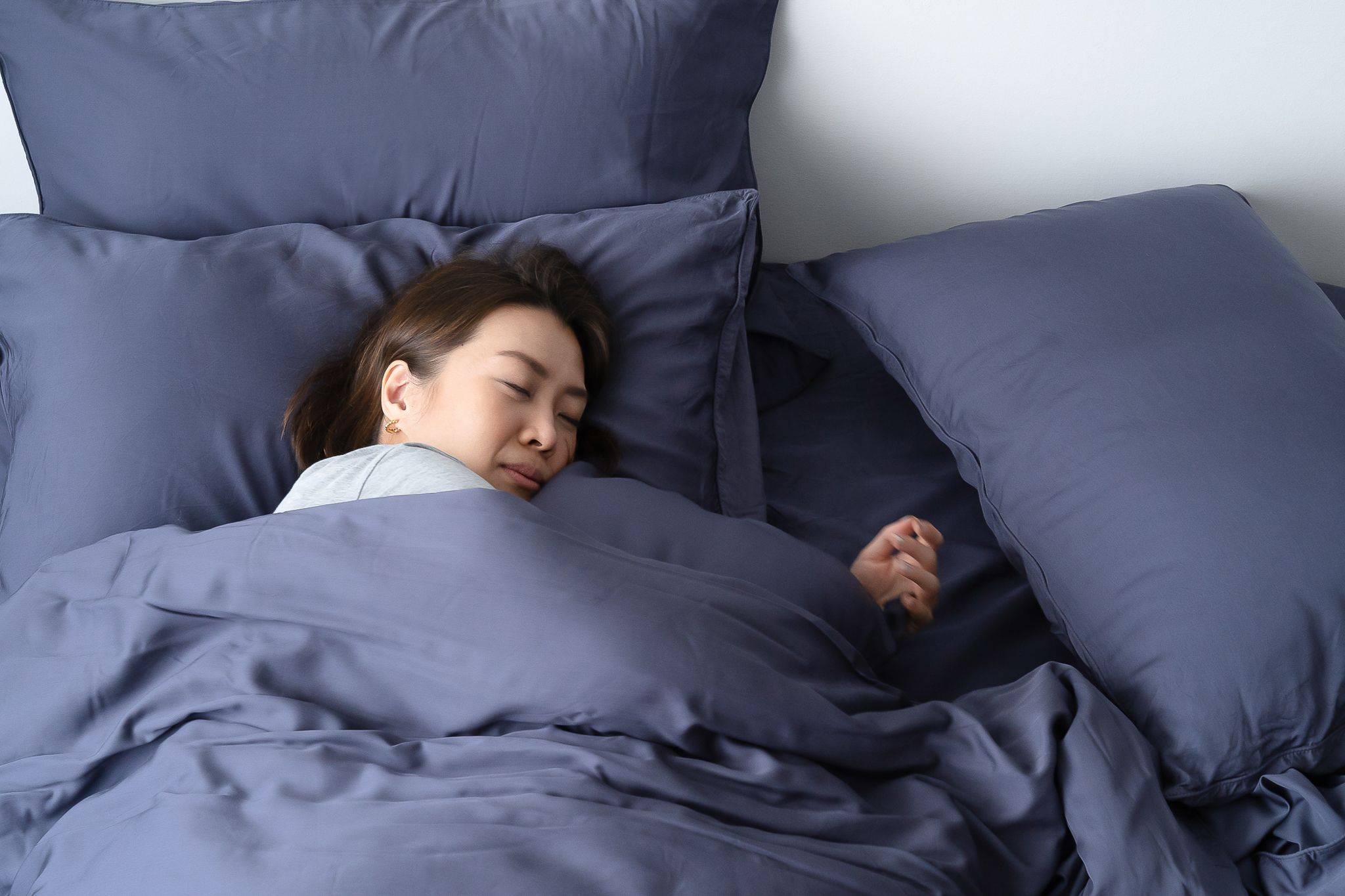 Woman sleeping in bed with Weavve's Tencel lyocell dark blue bed sheets