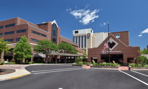 Hospital building with brick and modern design, surrounded by greenery, under a blue sky, evokes safety and hope.
