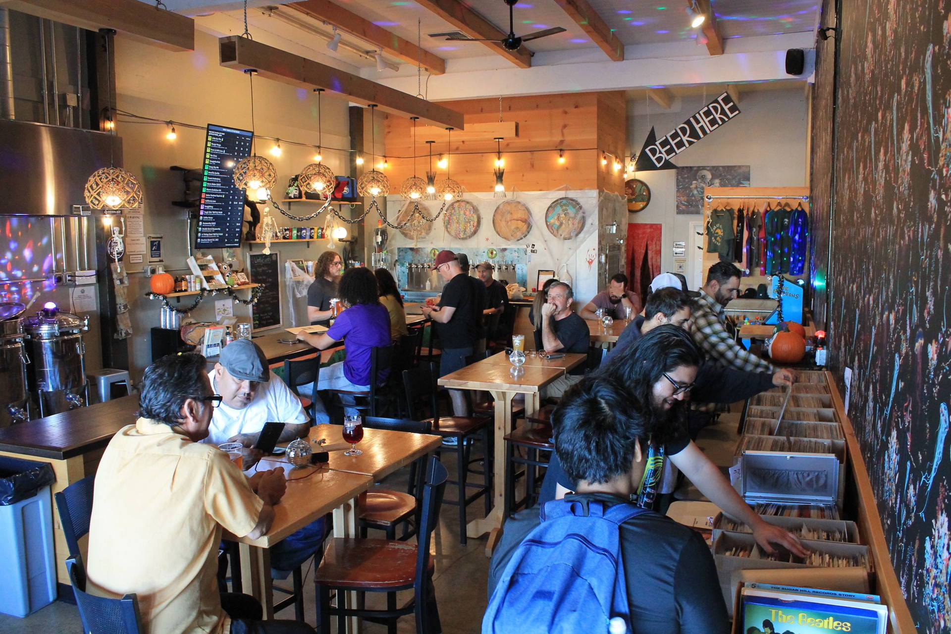 a wide angle view of Smog City West, showing hightop tables, a mural on the wall, low barrels and stools, and the bartop.