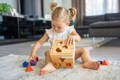 Little girl sitting on the carpet and inserting wooden shapes into the shape box. 