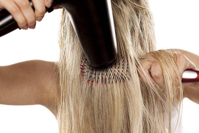 A woman blow drying her long blonde hair after applying styling cream