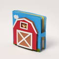 Blue felt farm busy book with a red barn, white door, and animal peeking through the window.