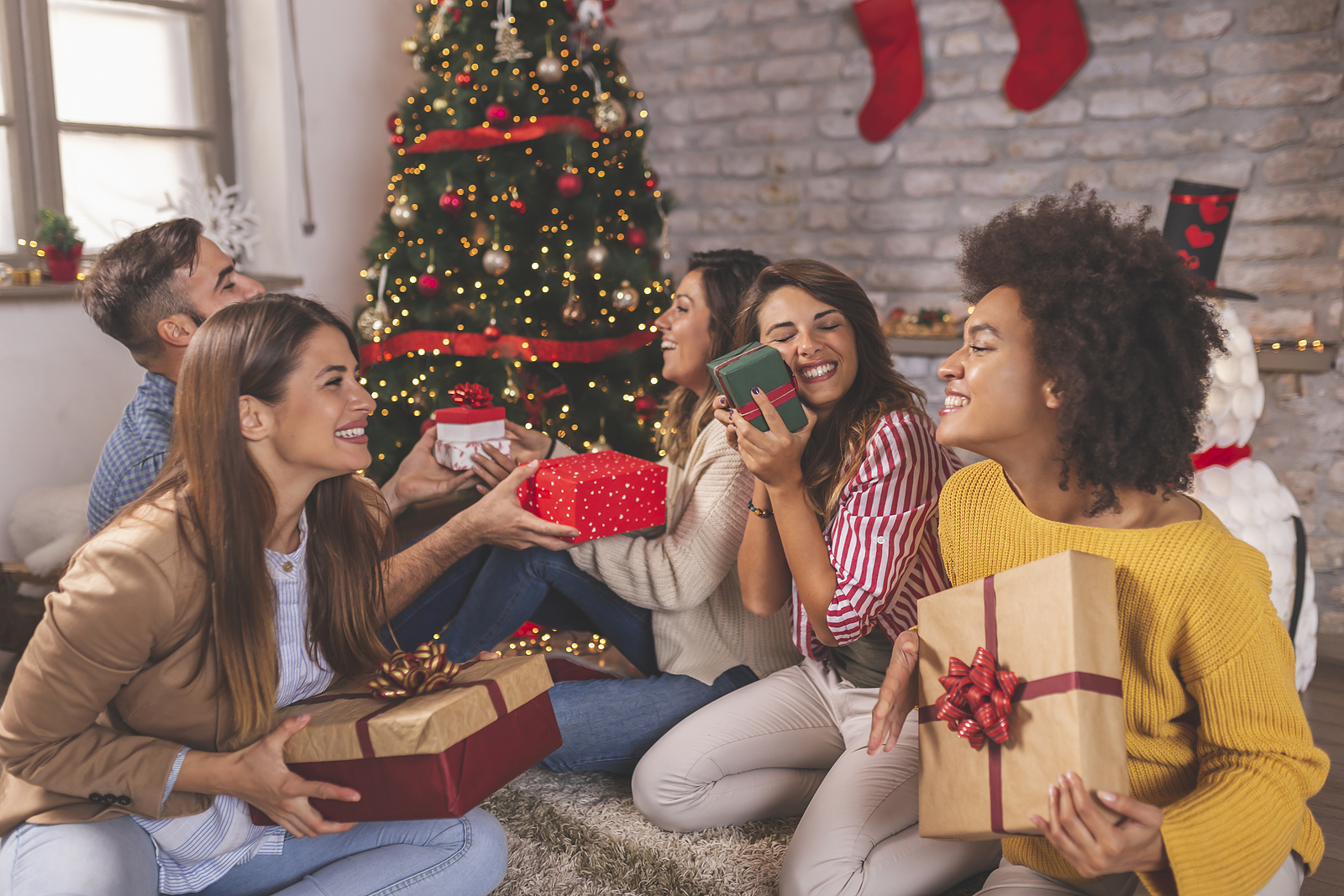 A group of several multi racial friends all exchanging gifts and smiling around the christmas tree.