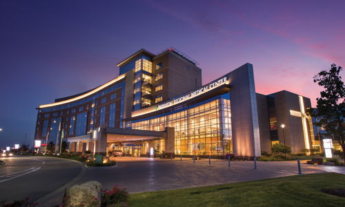 Modern building illuminated at dusk, featuring glass windows, greenery, and a calm twilight sky, evoking serenity and hospitality.