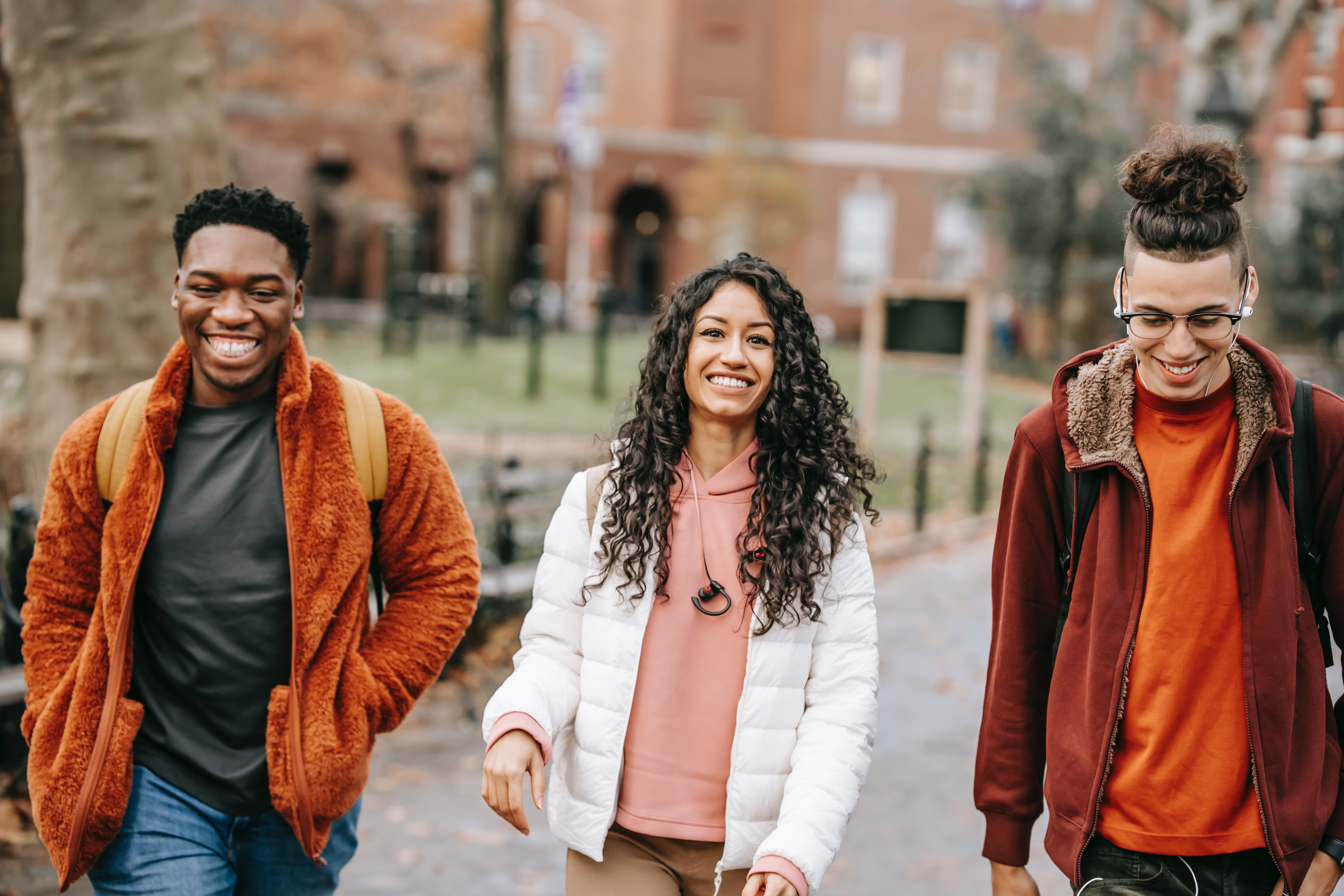A group of attractive friends smiling and walking together at a school campus wearing fall clothing.