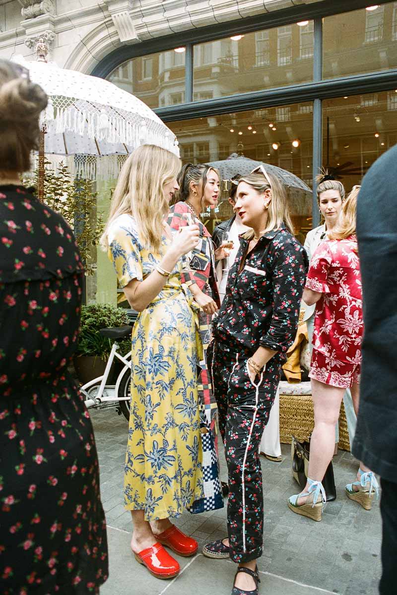Hermione Corfield and Gemma Sort-Chilvers chat at the YOLKE x Penelope Chilvers Launch aprty. Hermione Corfield wears YOLKE's Fan Print Sienna Dress and Gemma Sort-Chilvers wears YOLKE's Blossom Print Day Suit.