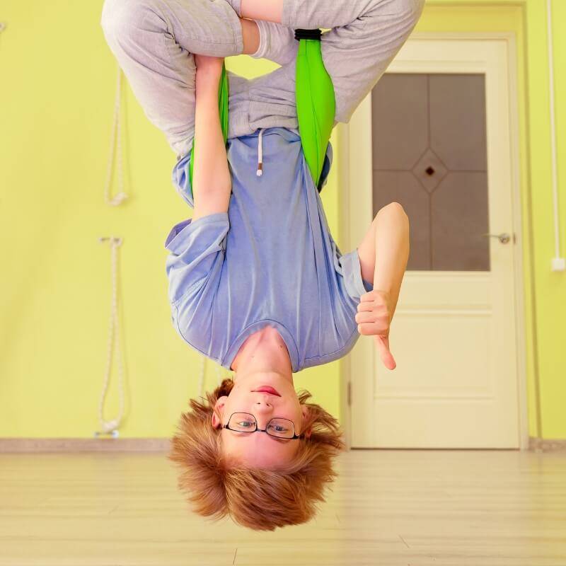 Boy with glasses hanging upside down on a sensory swing hammock.