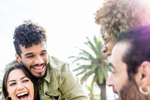 Two pairs of attractive couples laugh together while they carry their partners on their backs outdoors.