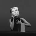 Model covering her face with a portrait of Debbie Harry behind a NOIRANCA handbag Debbie