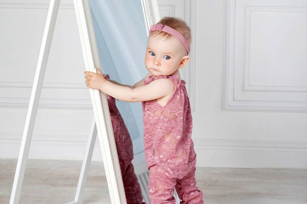 Cute baby girl standing in front of a tall mirror.
