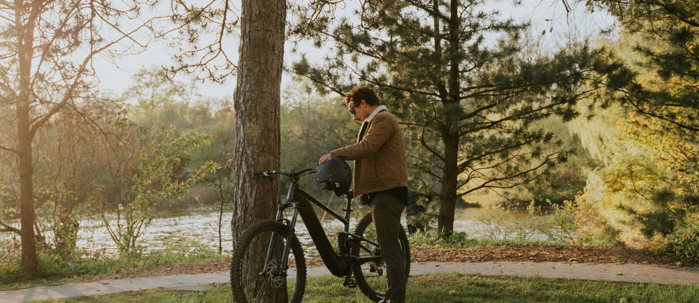 a man leaning a Giant Trance xE full suspension electric mountain bike against a tree