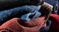 Foto von einem Stapel Pullovern, im Hintergrund Garne auf einer Spule