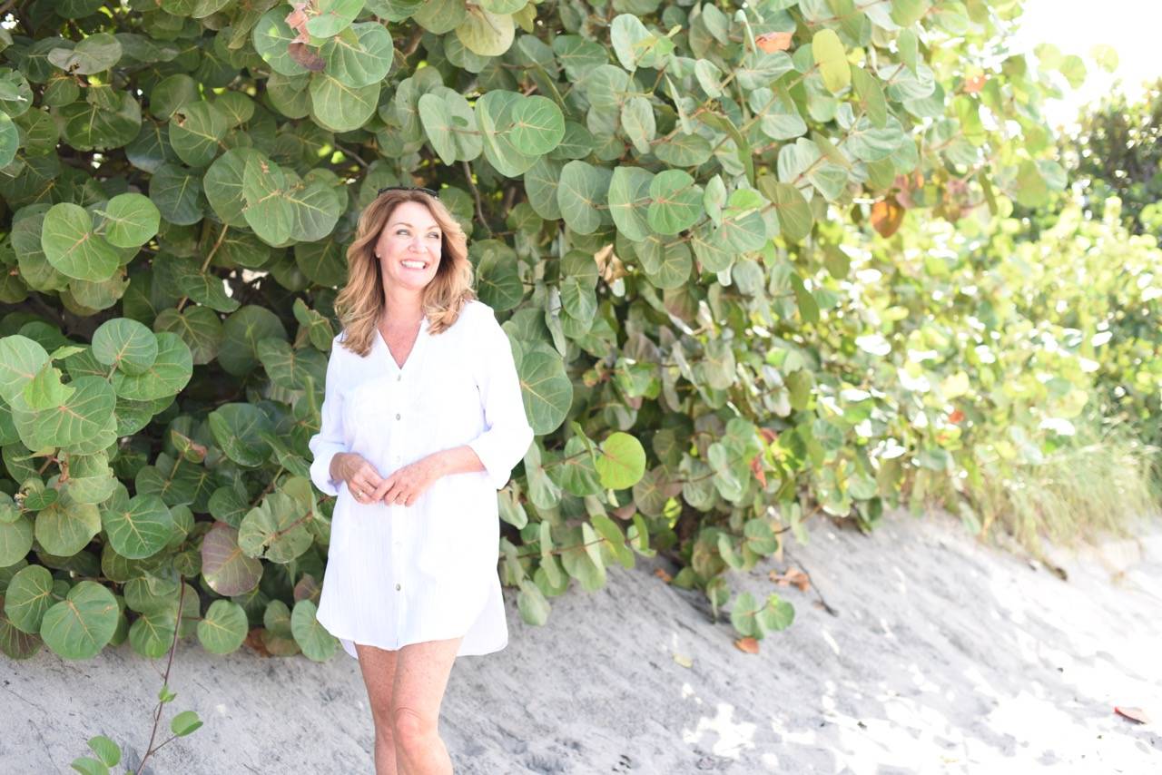 A woman wears a white button-front shirt cover-up on a beach.