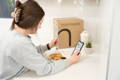 girl leaning on counter holding phone and ordering healthy meal prep while eating a healthy prepared meal