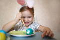 Little girl wearing plushy bunny ears painting an Easter egg.