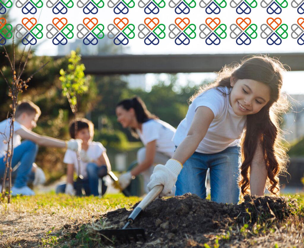 A smiling girl in a white shirt and jeans digs in the soil with a trowel, while other children and an adult plant trees in the background. Patterned heart designs border the top of the image.