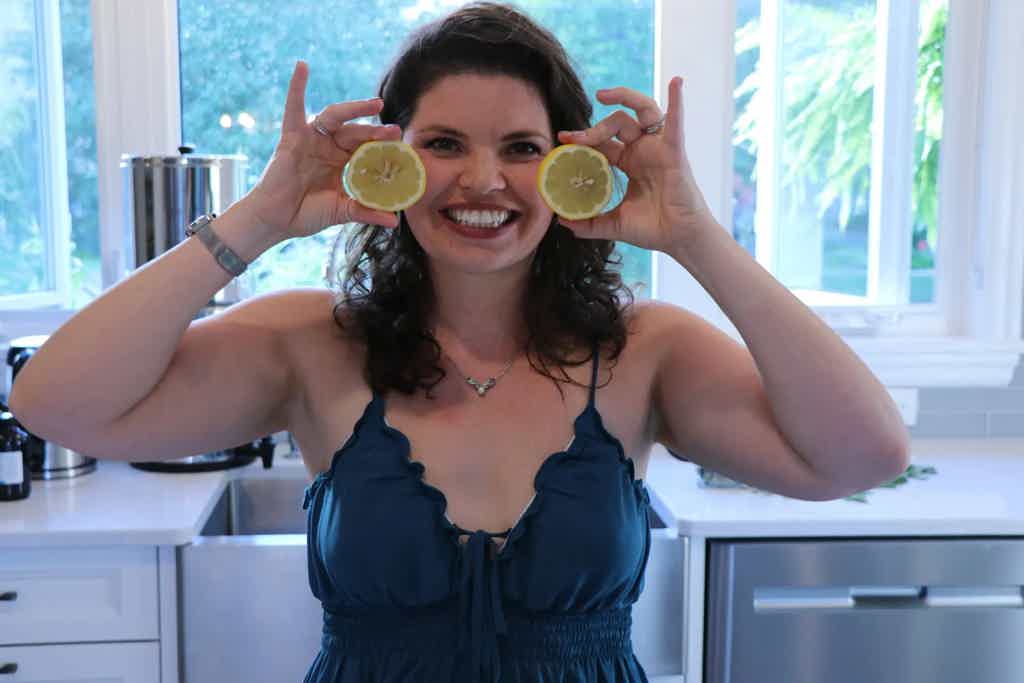 Dr. Keila in a kitchen holds two lemon slices over her eyes, playfully posing in front of a window with natural light.