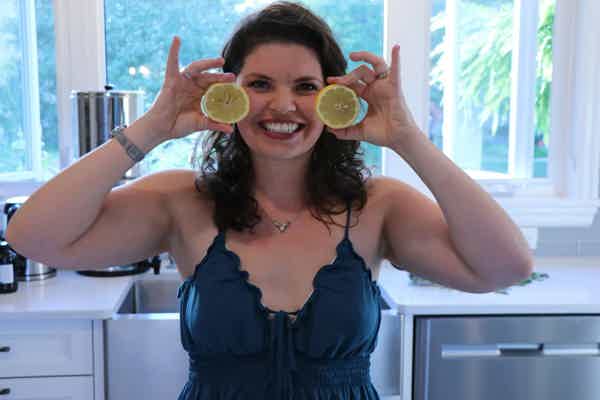 Dr. Keila in a kitchen holds two lemon slices over her eyes, playfully posing in front of a window with natural light.