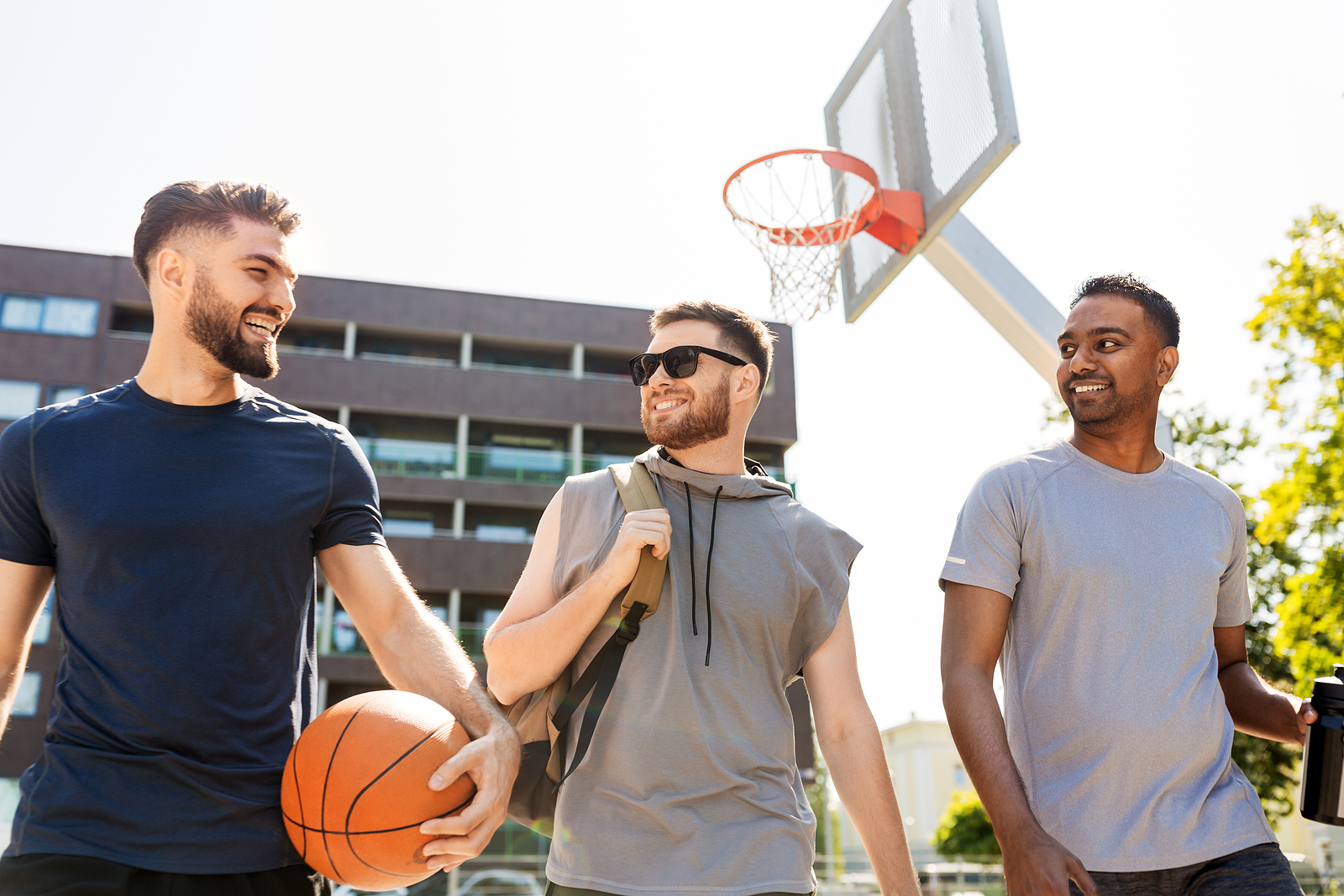 3 attractive guys wearing athletic clothes laughing while one is holding a basketball.