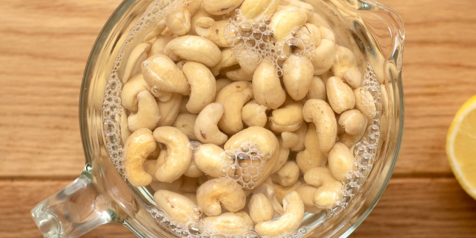 Measuring cup filled with cashews soaking in hot water.