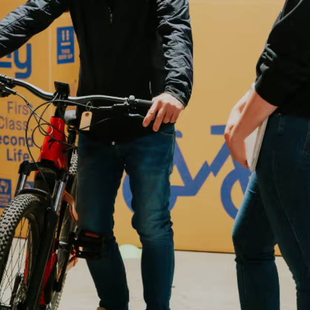 to men standing next to an electric mountain bike in front of upway bike boxes
