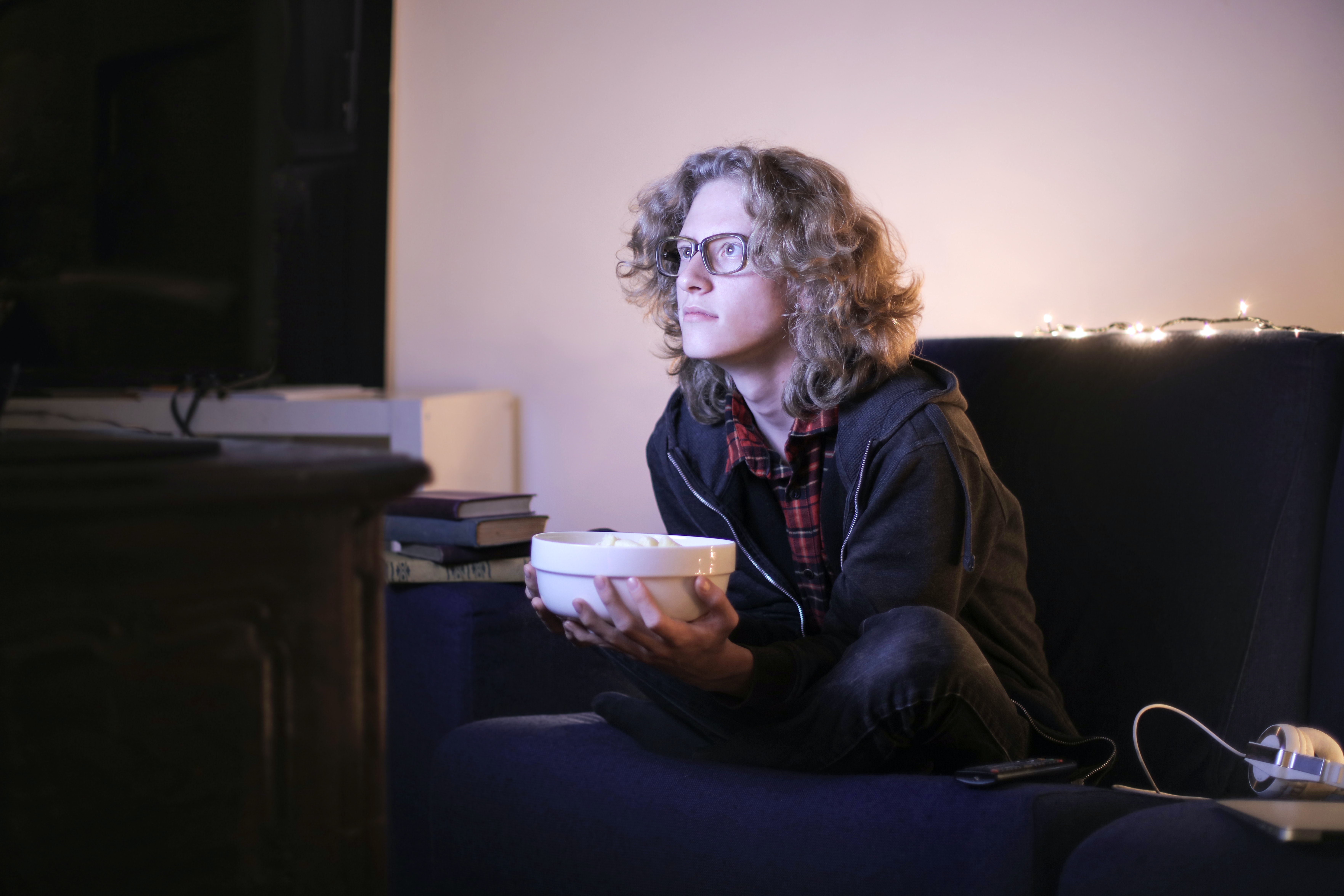 Image of a young white man with long hair and glasses looking intently at the t.v with a bowl of popcorn in his hands.
