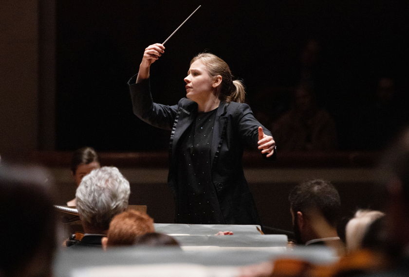Gemma New levantando un director de orquesta's batuta en su mano derecha. 