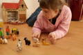 Young girl playing with wooden farm animal figures on the floor.