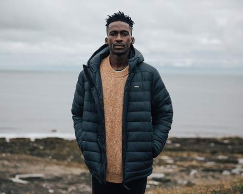 Black Finisterre Recycled Polyester Jacket Worn By Male Model With Sea Behind Him