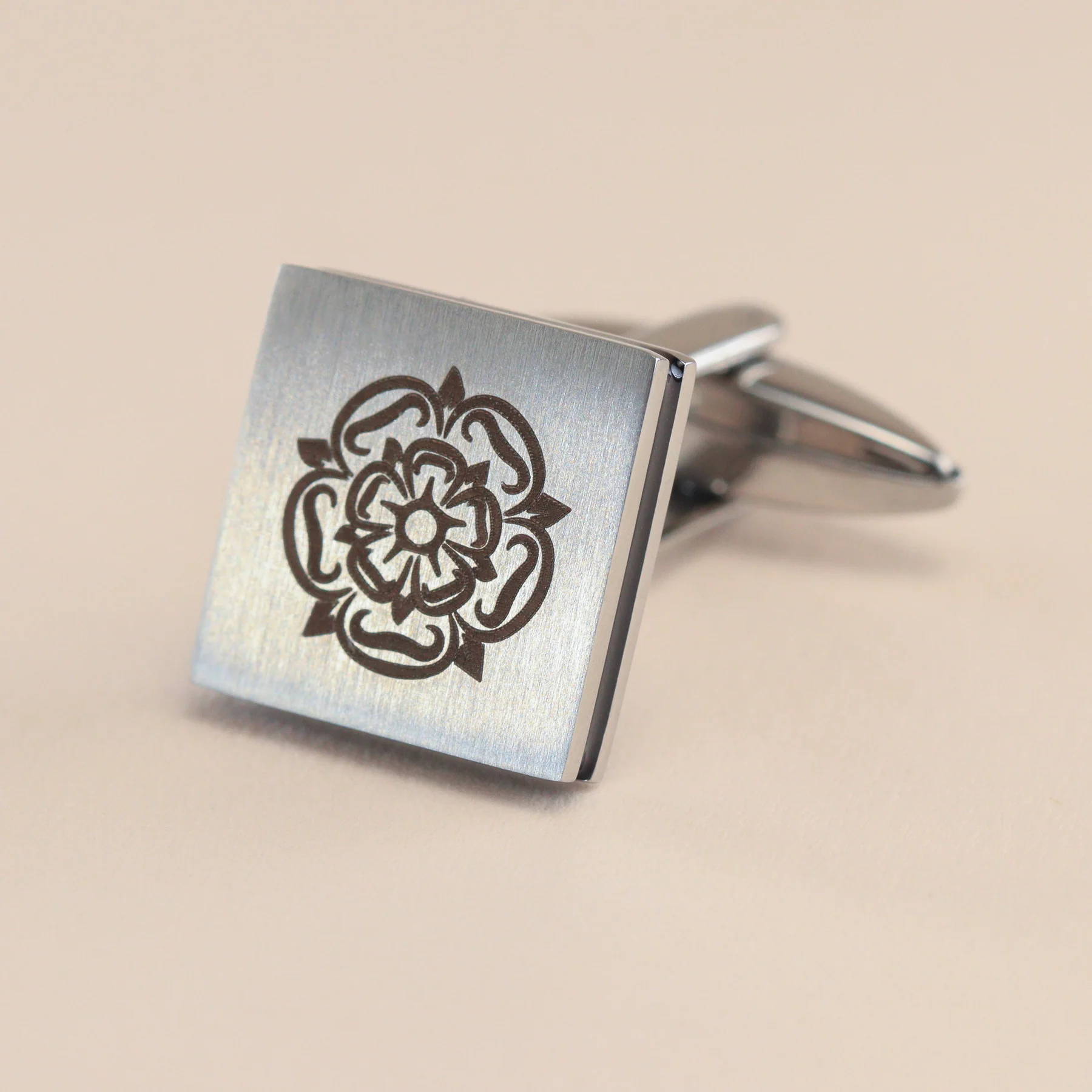 Close up image of a pair of polished stainless steel cufflinks with a Yorkshire Rose engraved on the face.