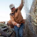 man using pocket knife to cut hay bale open