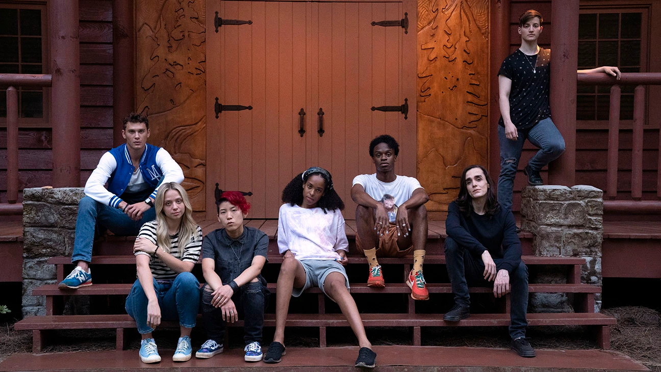 The teens in the camp sitting on the steps at the front door with serious expressions on their faces.