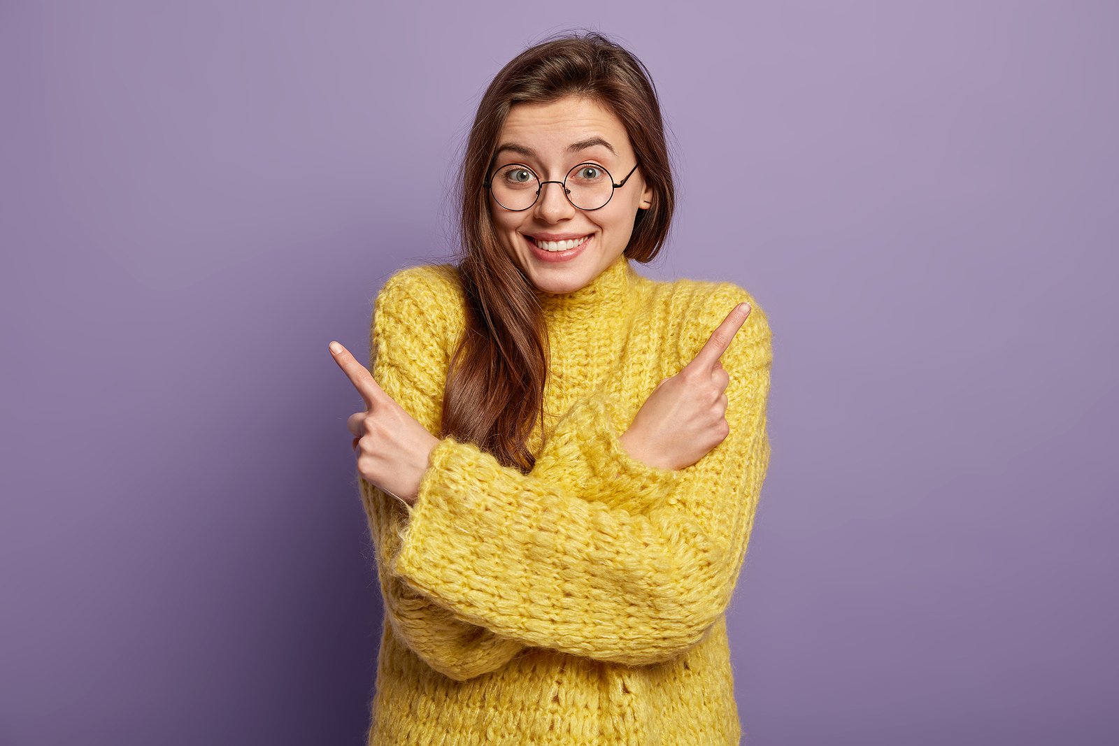 An attractive white woman wearing a knitted sweater smiles confused and points in both directions at the same time.