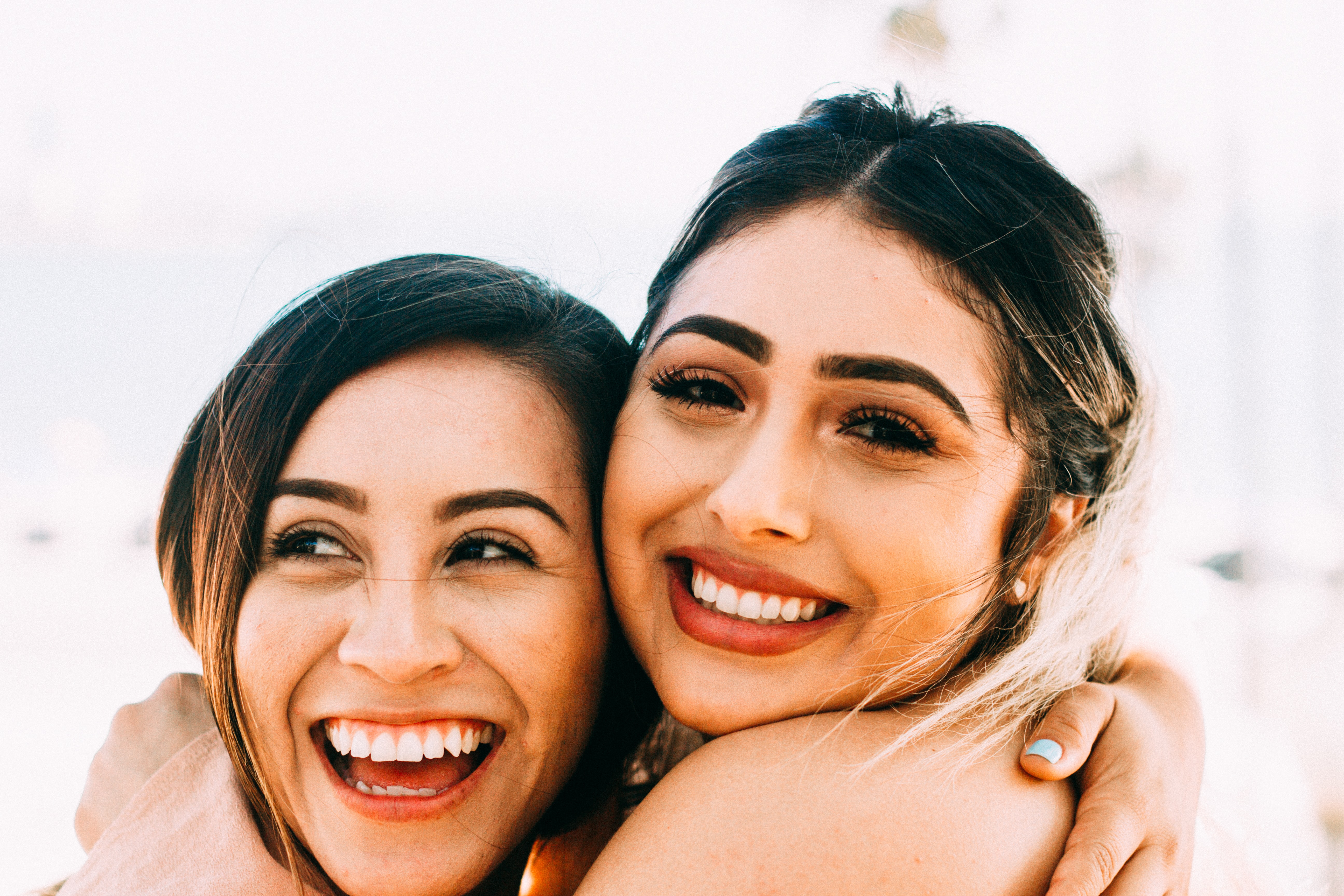 Two young latina women hugging and smiling looking at the camera