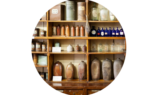 Wooden shelves filled with vintage apothecary jars and bottles in a historic pharmacy setting.