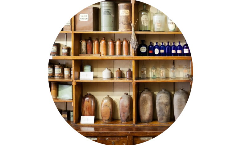 Wooden shelves filled with vintage apothecary jars and bottles in a historic pharmacy setting.