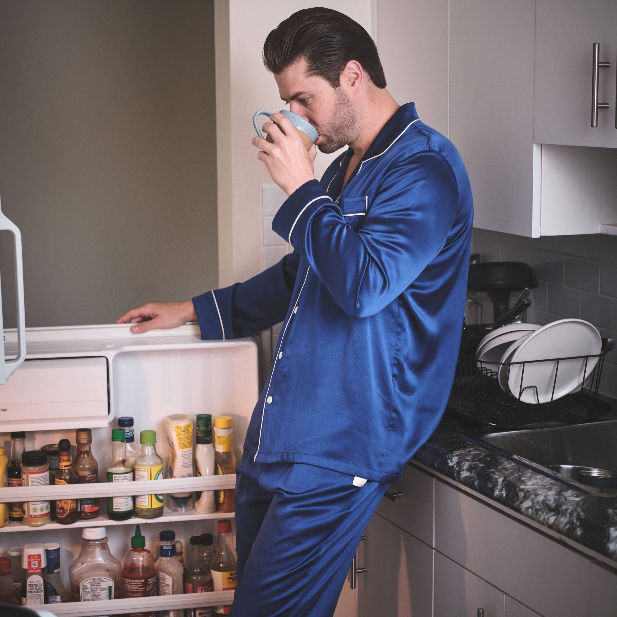 man looking for snacks in the fridge wearing a blue silk pajama set