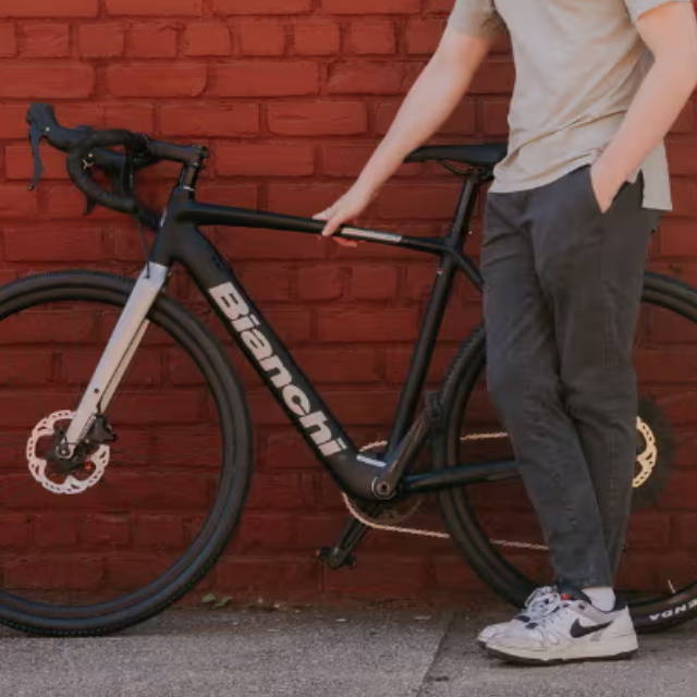 a man standing next to a bianchi electric road bike while standing in front of a red brick wall