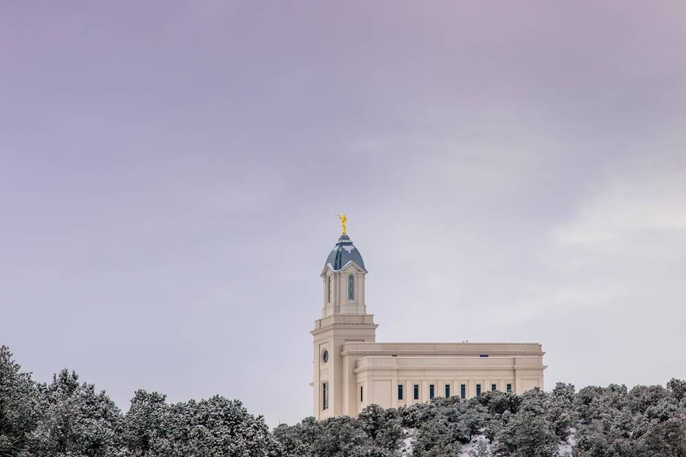 Distant photo of the Cedar City Temple standing above a wintery forest.