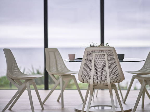 Five noho move chairs sitting around a glass table in front of a seaside