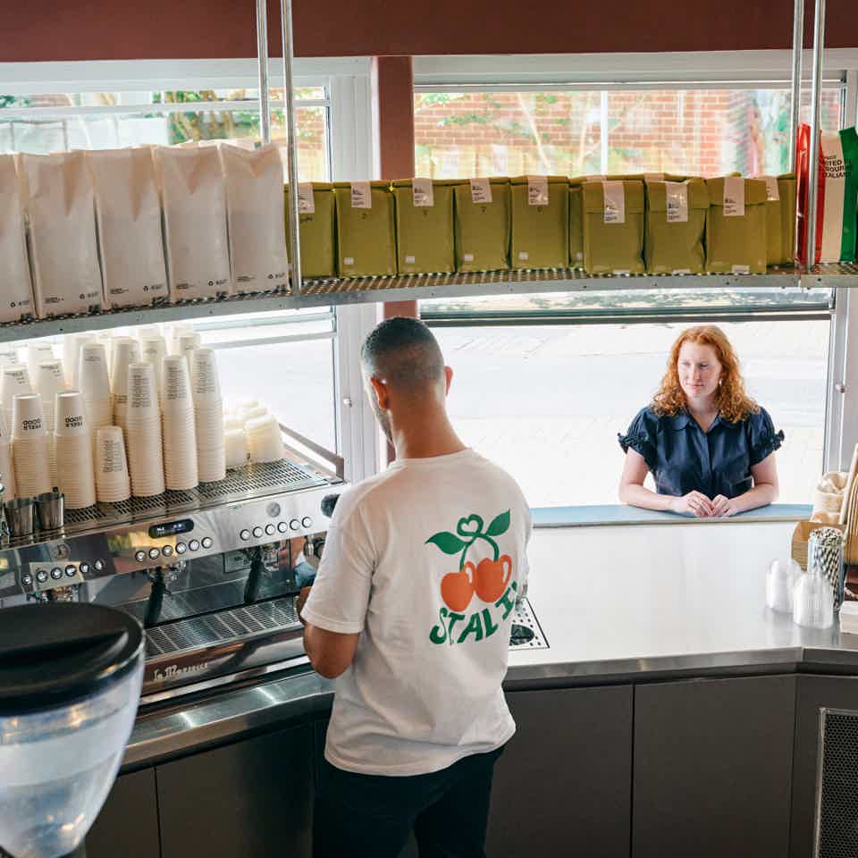 Barista working at a coffee machine behind a coutner while a lady waits